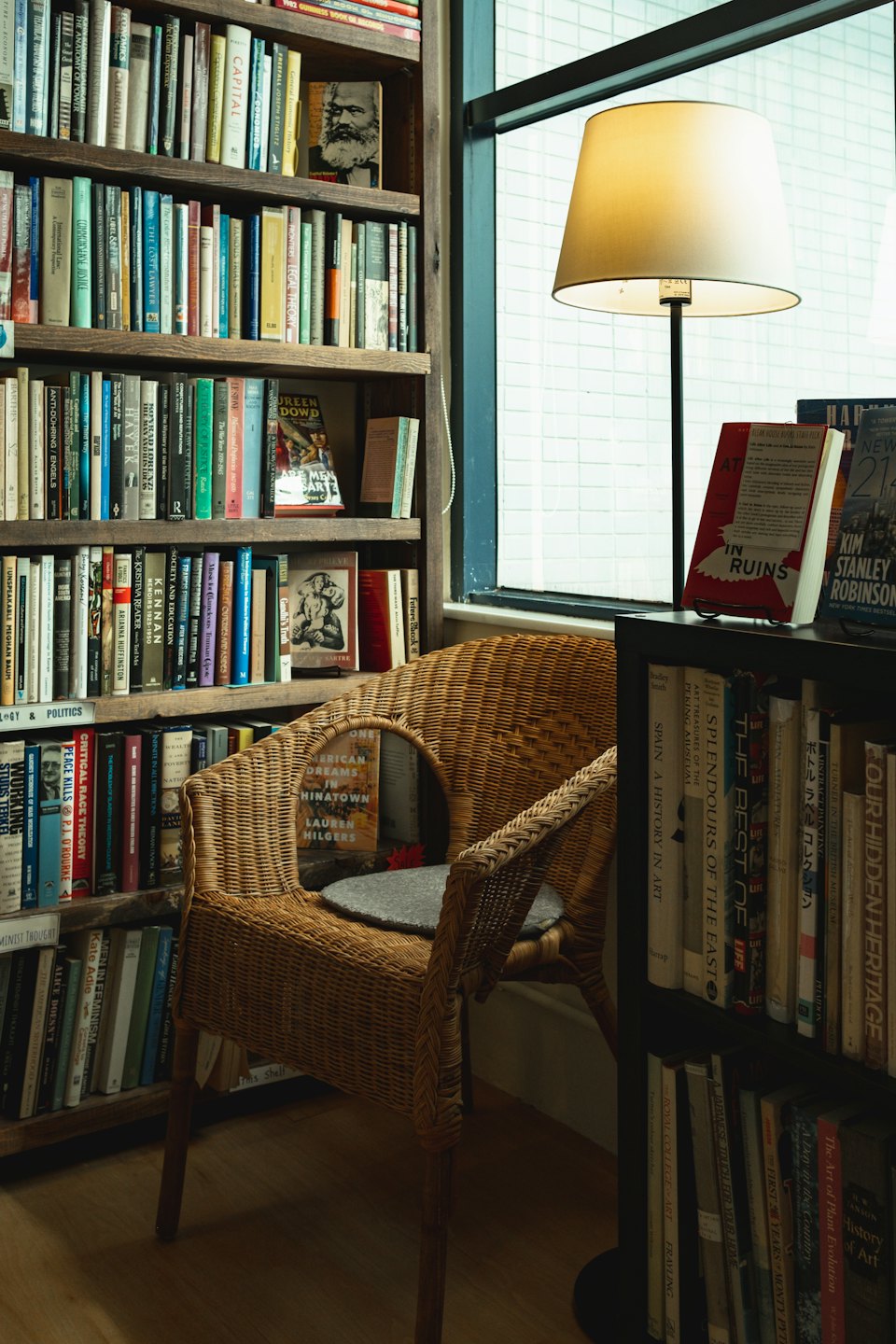 Cozy reading nook with a wicker armchair and bookshelf by the window.