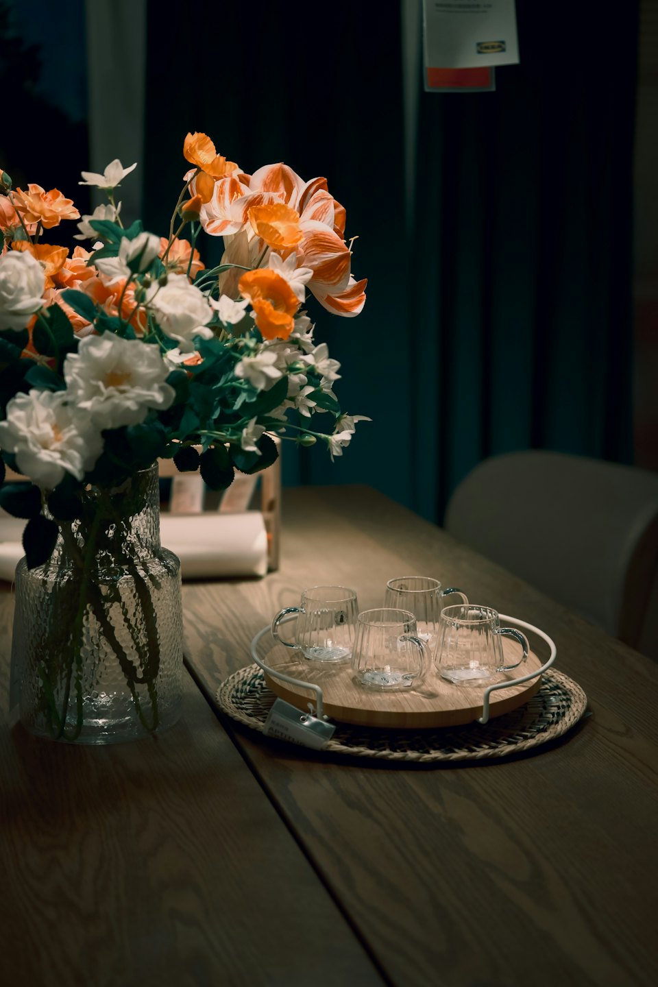 Glass vase with flowers on a wooden table with mugs.